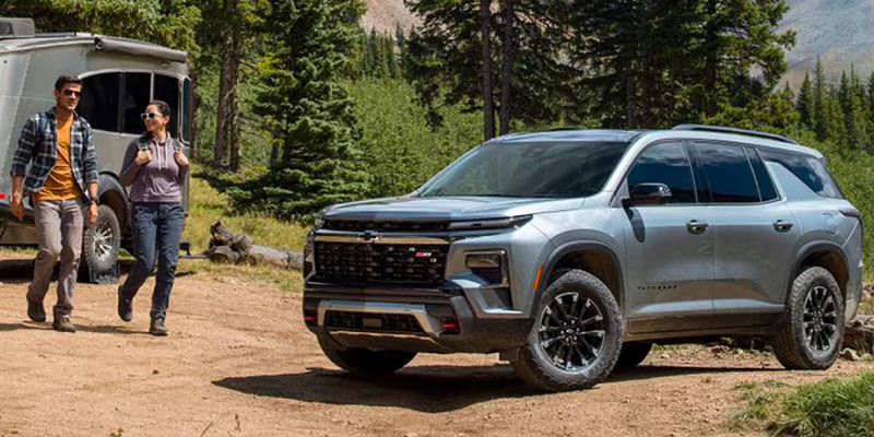 This image features a Chevrolet SUV in an outdoor setting, with two people walking towards the vehicle.