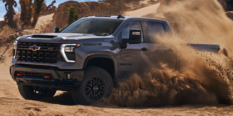 A Chevrolet Silverado HD kicking up dust as it powers through a rugged desert terrain.