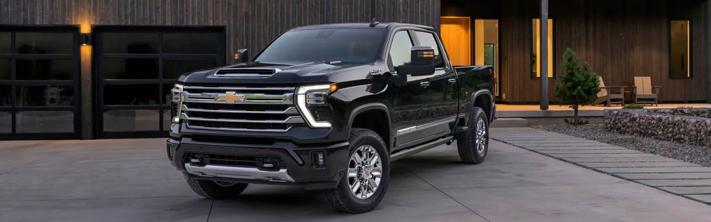 Black 2025 Chevy Silverado 2500 HD heavy-duty pickup truck parked in a modern driveway at dusk, showcasing its bold grille, large stance, and work-ready design.