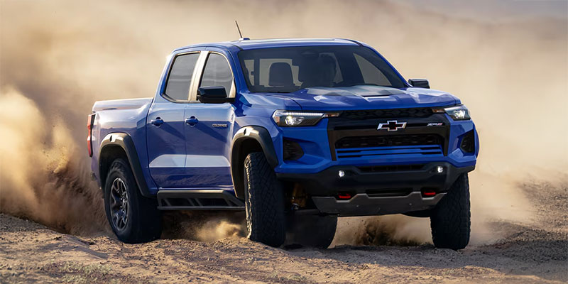 A blue 2025 Chevy Colorado driving through dusty terrain.