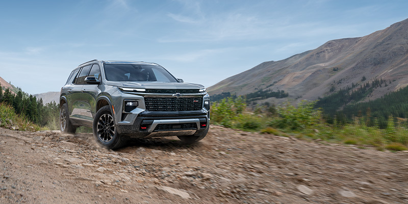 A rugged 2026 Chevrolet Traverse driving off-road through a mountainous terrain.