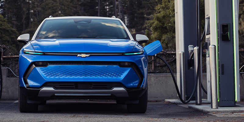Front view of a blue Chevrolet electric SUV charging at a public charging station.