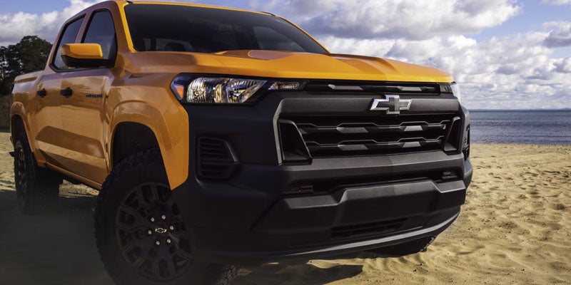 Front view of a yellow 2026 Chevrolet Colorado parked on the beach with a scenic sky in the background.