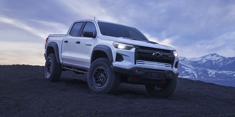 White 2026 Chevrolet Colorado parked on rugged terrain with a mountainous backdrop.
