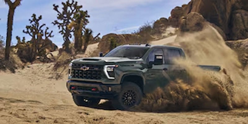 2026 Chevrolet Silverado 2500HD driving through desert terrain, kicking up dust.