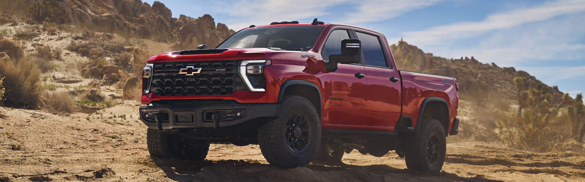 Red Chevrolet Silverado truck on a dirt road with mountains.
