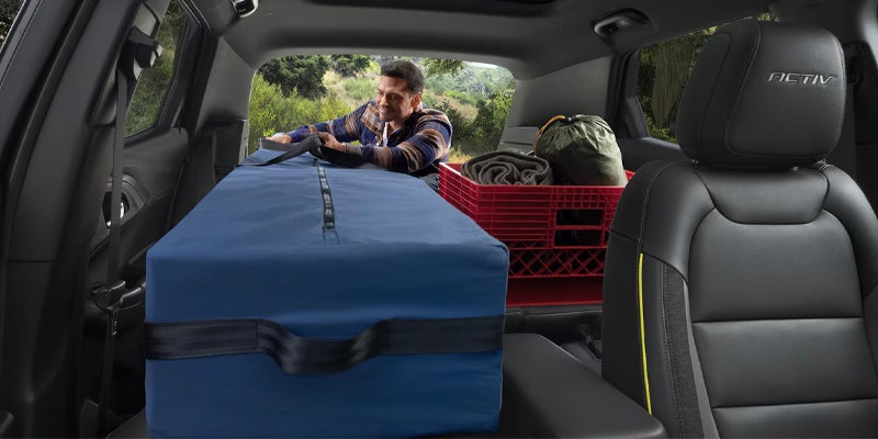 Cargo area of SUV loaded with storage bins and camping gear, with a person reaching in from outside.
