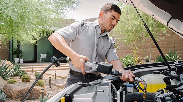A mechanic uses a power tool to work on a car engine outdoors.